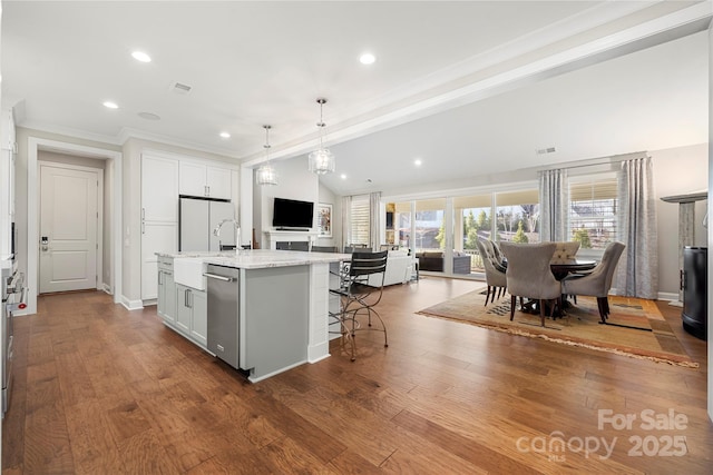 kitchen with lofted ceiling, white cabinetry, light stone counters, a center island with sink, and decorative light fixtures