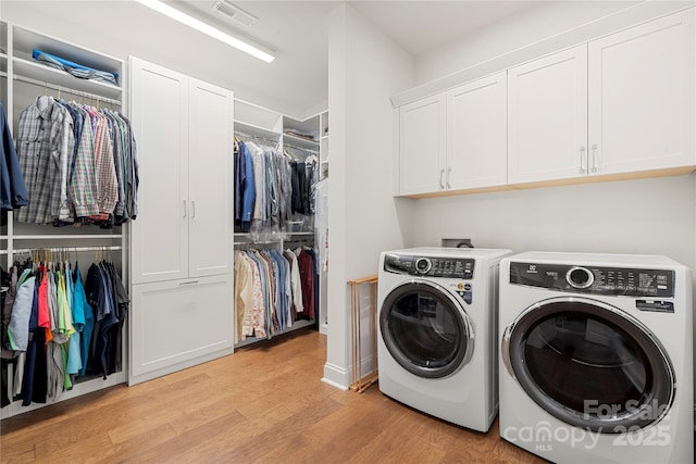 clothes washing area featuring washing machine and dryer, cabinets, and light wood-type flooring