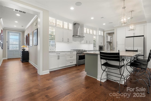 kitchen featuring wall chimney range hood, a kitchen island with sink, white cabinetry, stainless steel appliances, and light stone countertops