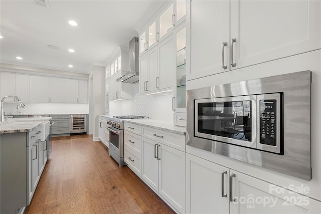 kitchen with stainless steel appliances, white cabinetry, light stone countertops, and wall chimney range hood