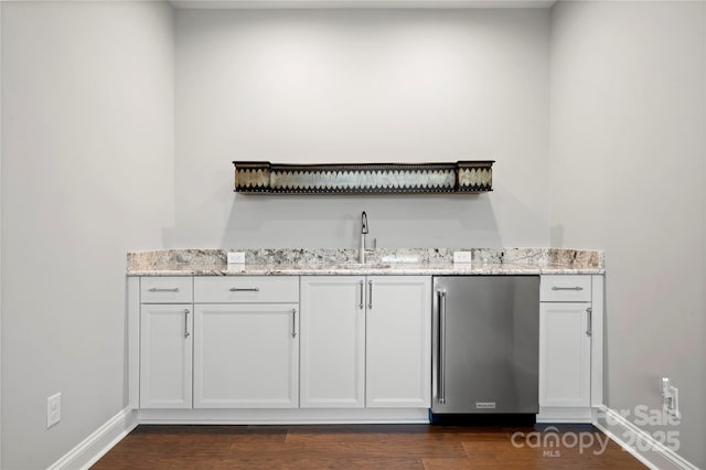 bar with white cabinetry, sink, stainless steel fridge, and light stone countertops