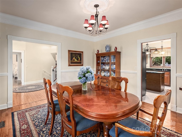 dining room featuring ornamental molding, a chandelier, sink, and light hardwood / wood-style flooring