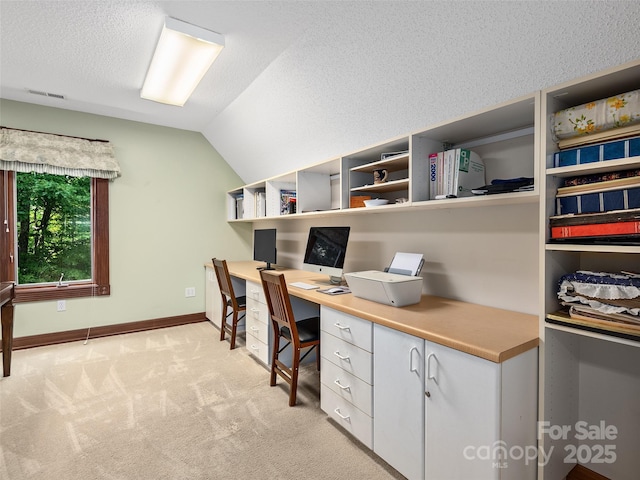 carpeted home office with lofted ceiling, built in desk, and a textured ceiling