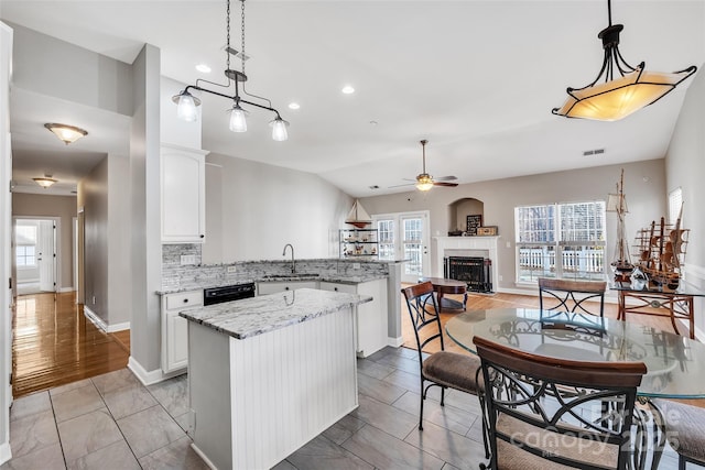 kitchen featuring sink, white cabinetry, a center island, hanging light fixtures, and light stone countertops