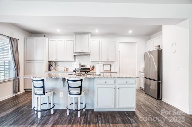 kitchen featuring white cabinetry, a center island with sink, appliances with stainless steel finishes, light stone countertops, and backsplash