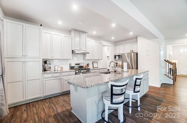 kitchen featuring a kitchen bar, a center island with sink, white cabinets, and appliances with stainless steel finishes