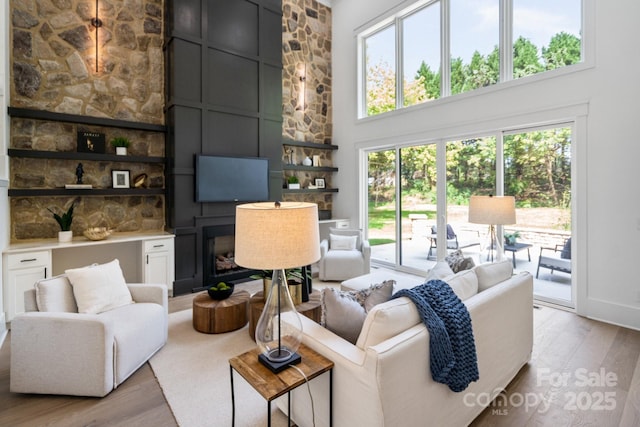 living room featuring a towering ceiling, a fireplace, and light wood-type flooring