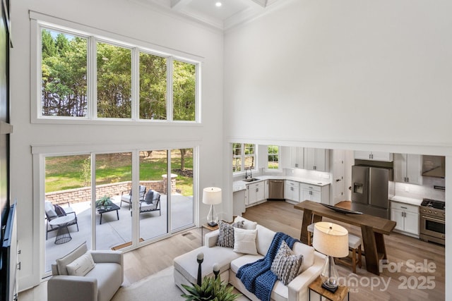 living room with beamed ceiling, coffered ceiling, a towering ceiling, and light wood-type flooring