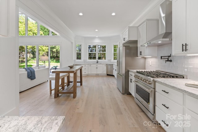 kitchen featuring backsplash, stainless steel appliances, light stone counters, white cabinets, and wall chimney exhaust hood