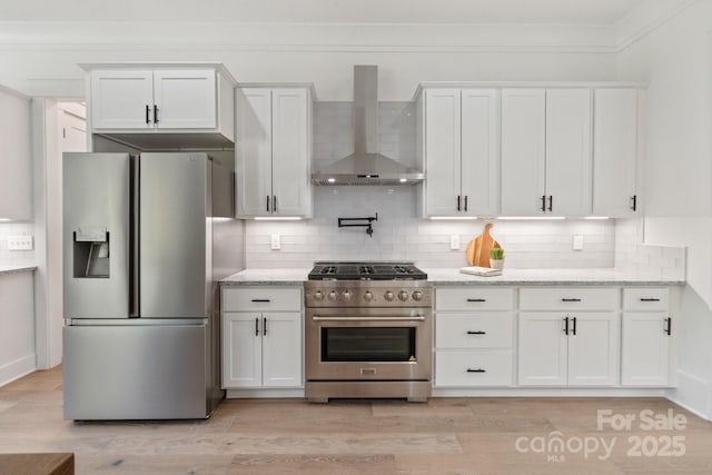 kitchen featuring wall chimney exhaust hood, stainless steel appliances, light stone counters, and white cabinets