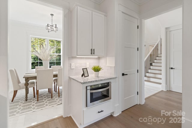 bar featuring tasteful backsplash, light hardwood / wood-style flooring, light stone countertops, oven, and white cabinets