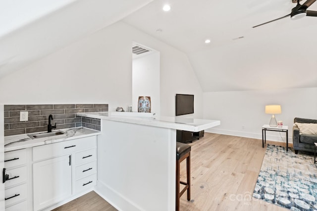 kitchen with sink, a breakfast bar area, white cabinets, kitchen peninsula, and light wood-type flooring