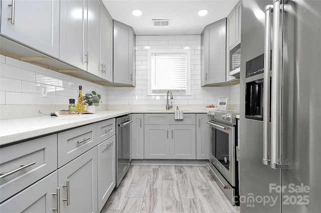 kitchen featuring sink, gray cabinetry, high quality appliances, light stone countertops, and decorative backsplash