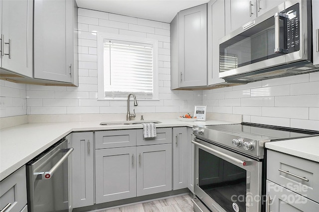 kitchen featuring tasteful backsplash, stainless steel appliances, gray cabinets, and sink