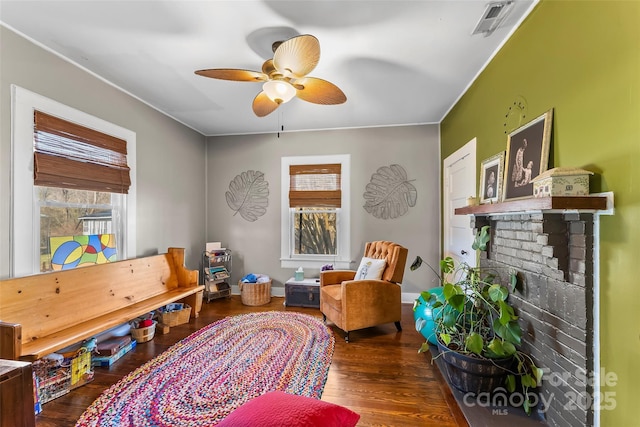 living area featuring ceiling fan, dark wood-type flooring, a healthy amount of sunlight, and a brick fireplace