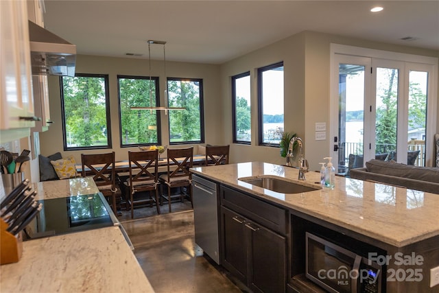 kitchen featuring decorative light fixtures, an island with sink, sink, stainless steel dishwasher, and light stone counters