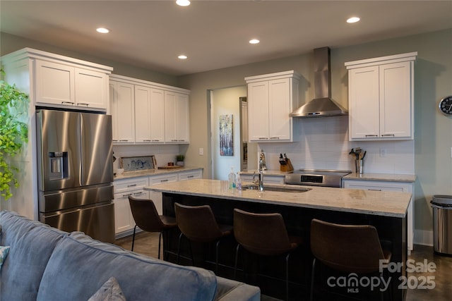 kitchen featuring appliances with stainless steel finishes, a kitchen island with sink, white cabinets, and wall chimney exhaust hood