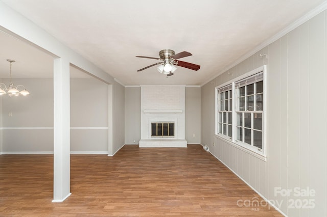 unfurnished living room featuring ceiling fan with notable chandelier, ornamental molding, hardwood / wood-style floors, and a brick fireplace