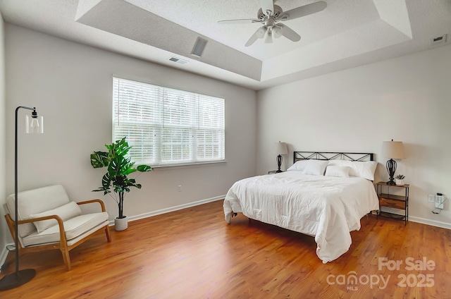 bedroom featuring wood-type flooring, ceiling fan, and a tray ceiling