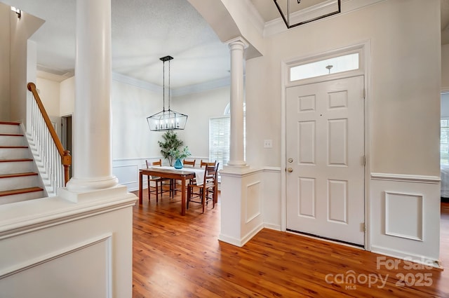 foyer entrance with hardwood / wood-style floors, a chandelier, decorative columns, and ornamental molding