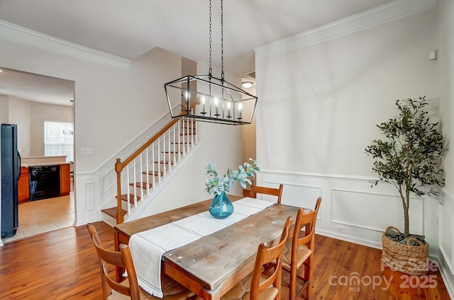 dining space with hardwood / wood-style flooring, ornamental molding, and an inviting chandelier