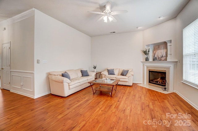 living room with light wood-type flooring, ceiling fan, and a fireplace