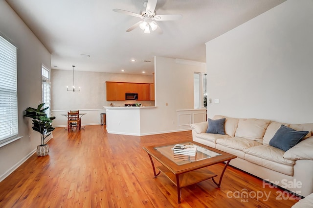 living room featuring ceiling fan with notable chandelier and light hardwood / wood-style flooring