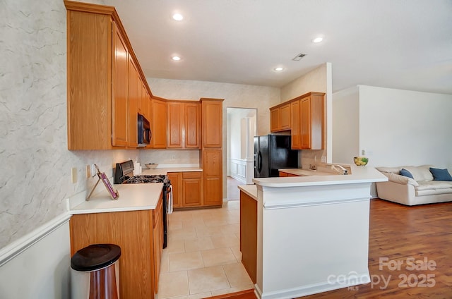 kitchen featuring a kitchen bar, backsplash, black appliances, and kitchen peninsula