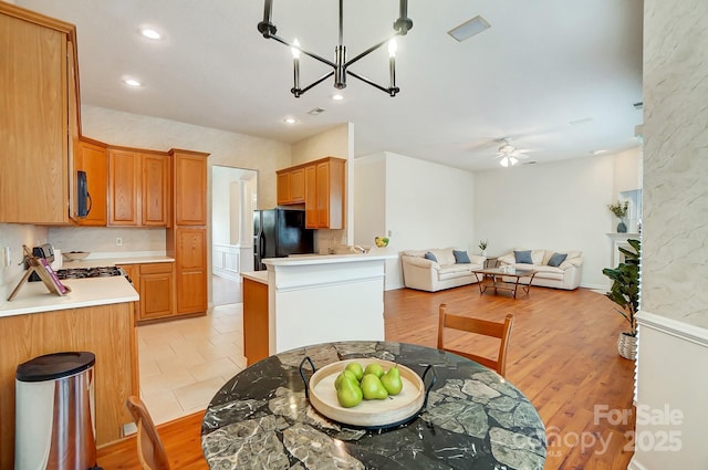 kitchen with ceiling fan with notable chandelier, light hardwood / wood-style floors, black appliances, and decorative backsplash