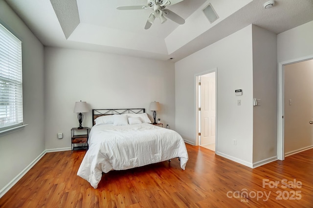 bedroom featuring a tray ceiling, ceiling fan, and light wood-type flooring