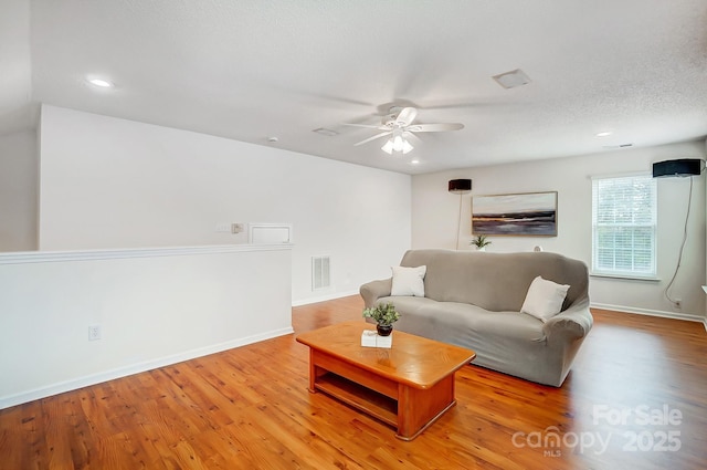 living room featuring light wood-type flooring, ceiling fan, and a textured ceiling