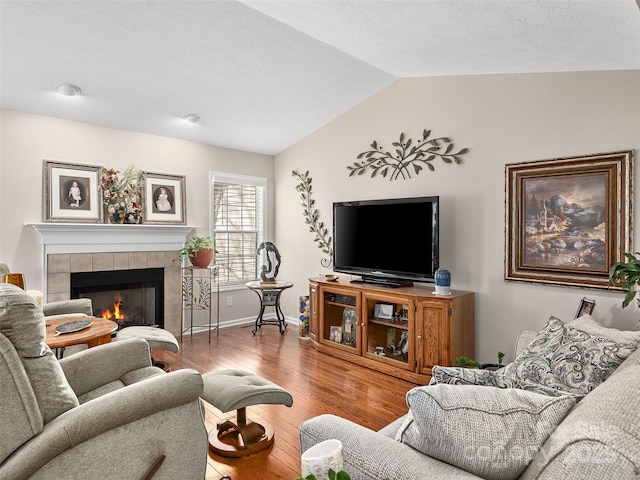 living room with lofted ceiling, a tile fireplace, and wood-type flooring