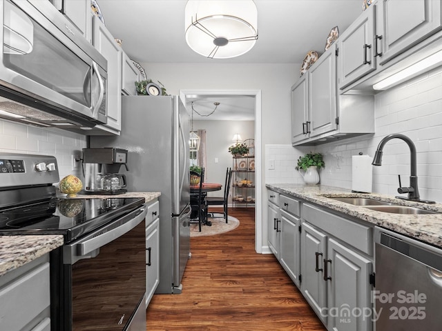 kitchen featuring sink, tasteful backsplash, light stone counters, appliances with stainless steel finishes, and dark hardwood / wood-style floors