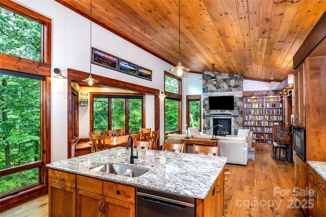 kitchen with sink, a kitchen island with sink, light stone counters, a stone fireplace, and decorative light fixtures