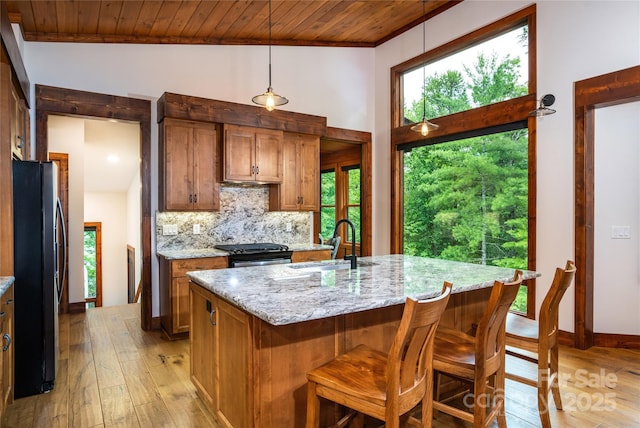 kitchen featuring pendant lighting, sink, black refrigerator, light stone countertops, and an island with sink