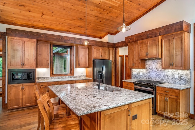 kitchen featuring decorative light fixtures, built in microwave, stainless steel fridge, a kitchen island with sink, and gas range