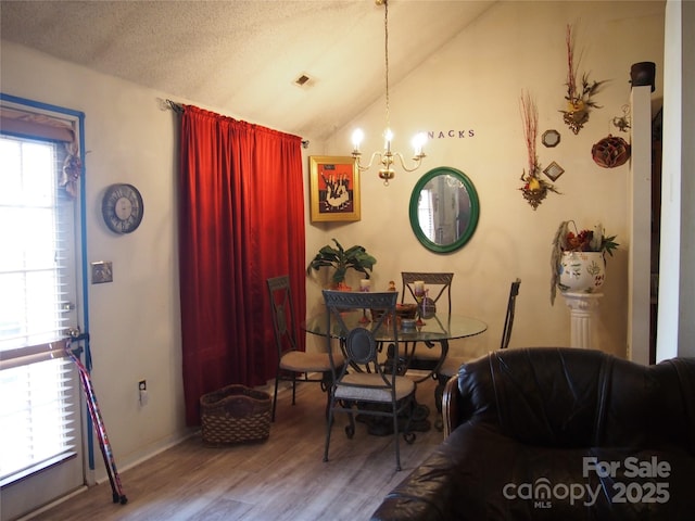 sitting room with wood-type flooring, a chandelier, vaulted ceiling, and a textured ceiling