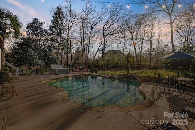 pool at dusk featuring a patio area, a hot tub, and pool water feature