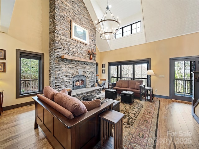 living room with a notable chandelier, a stone fireplace, high vaulted ceiling, and light wood-type flooring