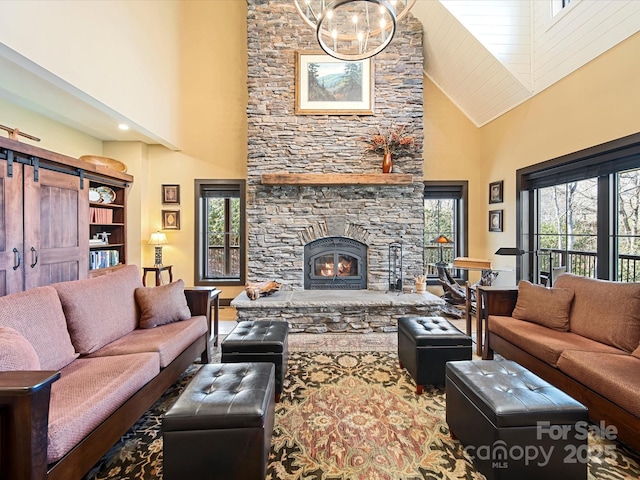 living room featuring an inviting chandelier, a towering ceiling, and a stone fireplace