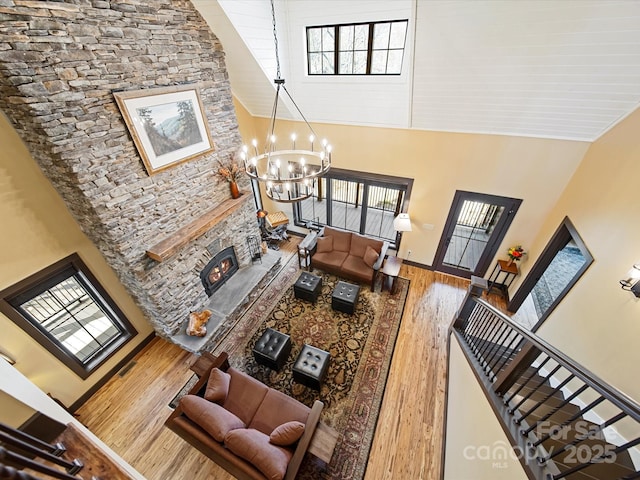 living room with wood-type flooring, a towering ceiling, an inviting chandelier, and a fireplace