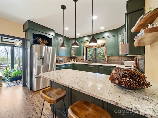 kitchen featuring stainless steel fridge with ice dispenser, pendant lighting, sink, green cabinetry, and light stone countertops