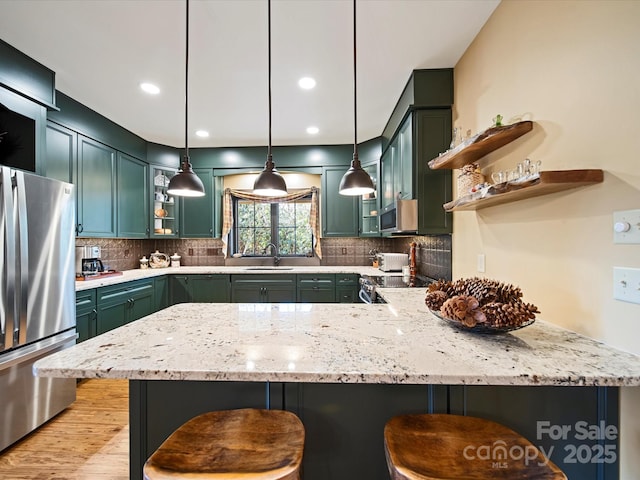 kitchen featuring a breakfast bar area, green cabinets, appliances with stainless steel finishes, light stone counters, and kitchen peninsula