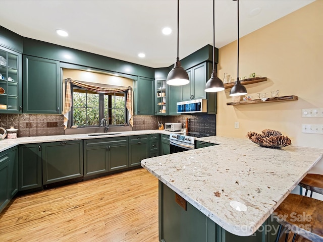 kitchen with pendant lighting, stainless steel appliances, kitchen peninsula, and green cabinets