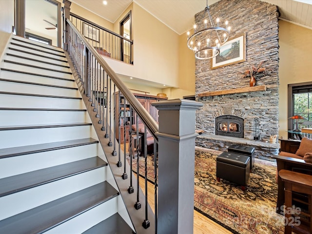 stairway with hardwood / wood-style floors, ceiling fan with notable chandelier, a fireplace, and high vaulted ceiling