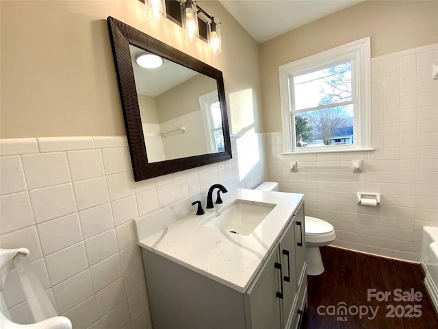 bathroom featuring wood-type flooring, tile walls, vanity, and toilet