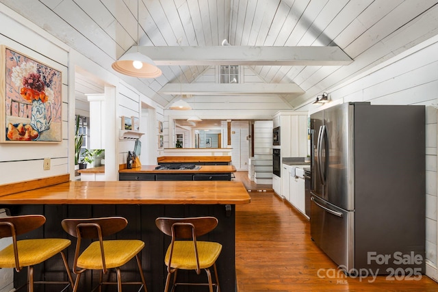 kitchen featuring lofted ceiling with beams, wood counters, dark wood-type flooring, black appliances, and a kitchen bar