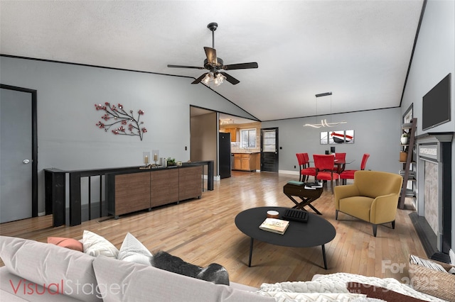 living room with lofted ceiling, a fireplace, ceiling fan, and light wood-type flooring