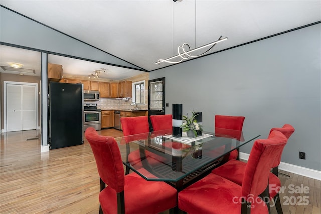 dining room with lofted ceiling, sink, a chandelier, and light hardwood / wood-style floors