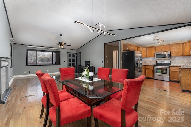 dining area with lofted ceiling, ceiling fan with notable chandelier, a textured ceiling, and light wood-type flooring